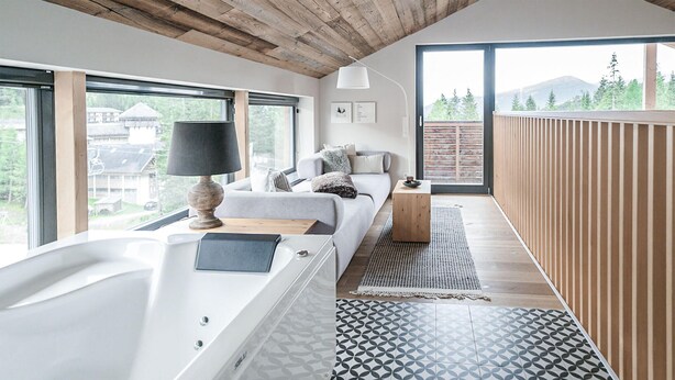Ein modernes Schlafzimmer mit großem Fenster, Holzboden, einem Bett mit Kissen, einem Nachttisch und einem gemusterten Teppich.