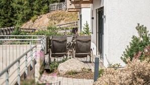 Ein Außenbereich mit Sitzgelegenheiten, einem Tisch, einem großen Felsen und einem weißen Gebäude mit Balkon.