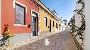 A cobblestone street lined with buildings featuring traditional architecture, a narrow alley, and a small plant with flowers. - Villa 'Bougainvillea House' with Balcony, Wi-Fi and Air Conditioning (Faro)