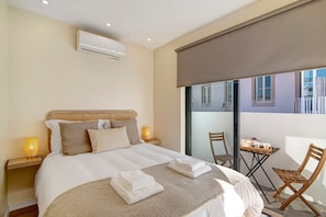 A hotel room with a bed, bedside tables, a small table with chairs, and a window with a view.