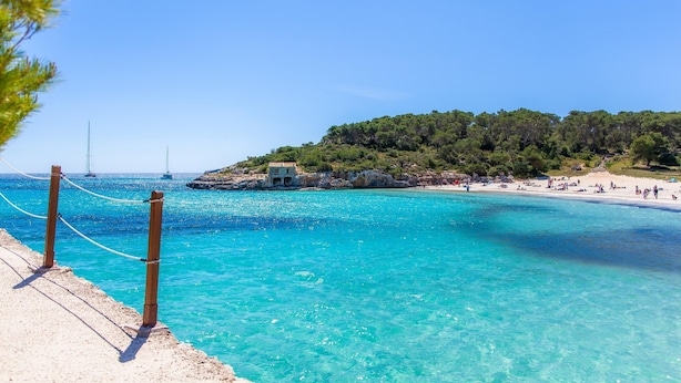 A beach with clear turquoise water, a sandy shore, and a small building on a hill. - Villa 'Amarador' with Private Pool, Wi-Fi and Air Conditioning (Santanyí)