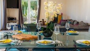A dining area with a glass table, chairs, a bowl of flowers, and a sofa in the background. - Villa 'Amarador' with Private Pool, Wi-Fi and Air Conditioning (Santanyí)