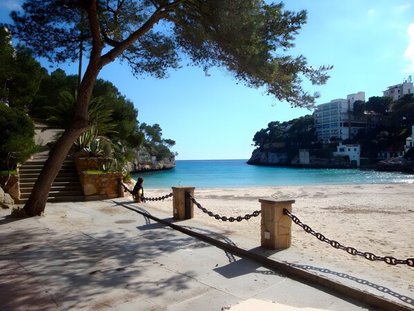 A beach with a chain barrier, stairs leading down to the water, and buildings on a cliff in the background.