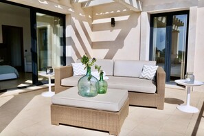 A modern outdoor seating area with wicker furniture, two glass vases with plants, and a white table.