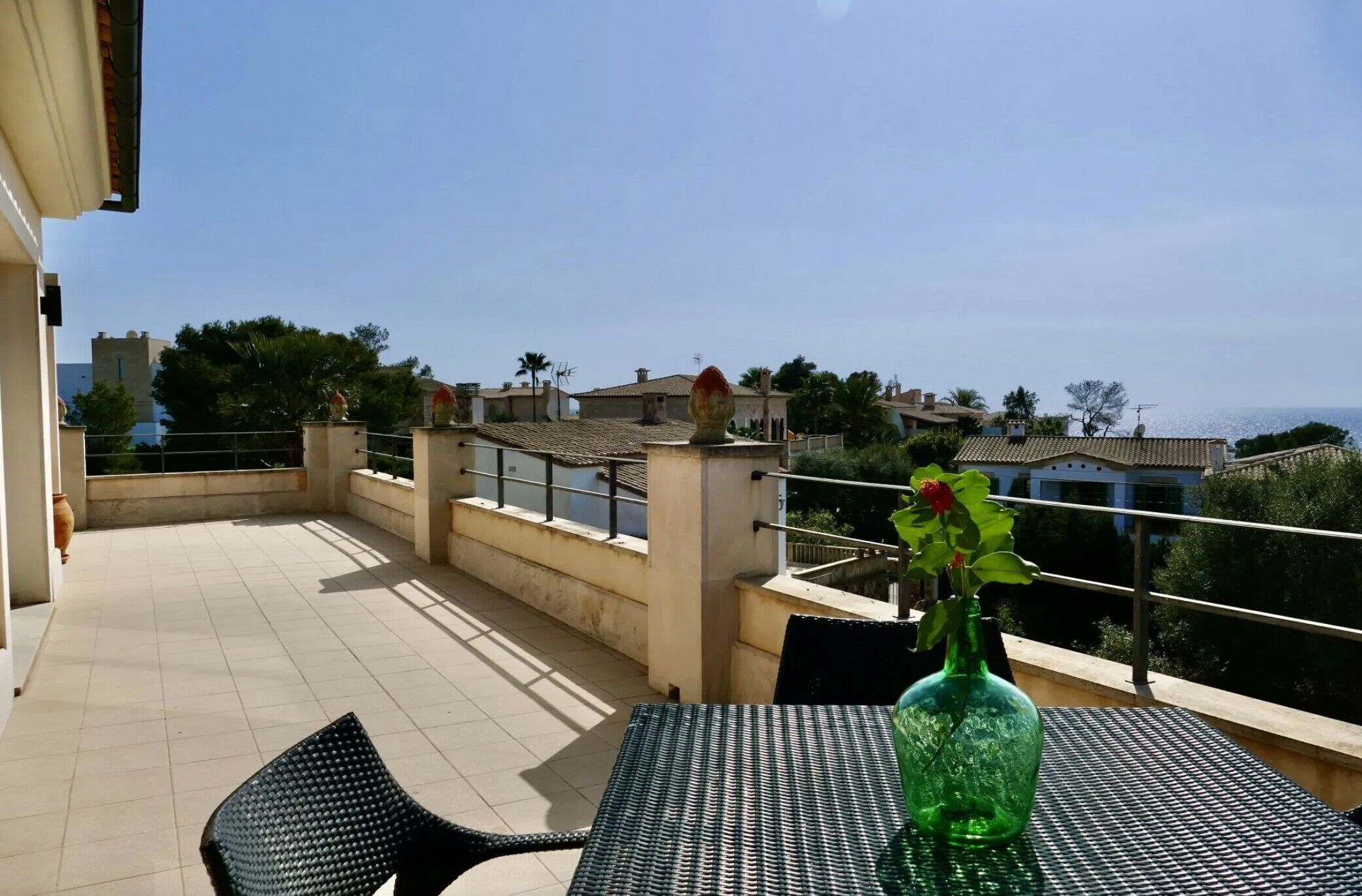 A terrace with a table, chairs, and a green bottle with flowers.