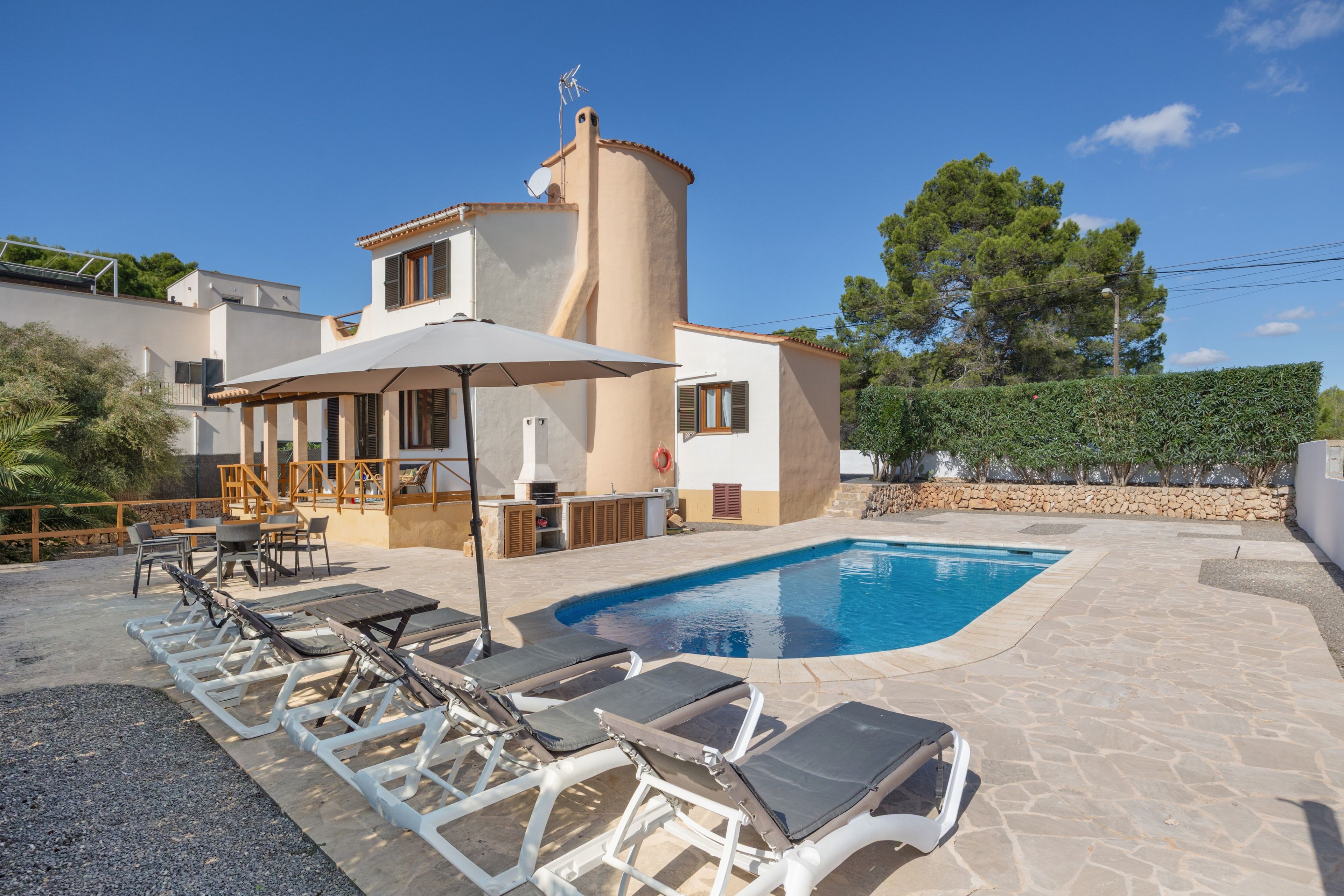 Una casa de dos pisos con piscina, mobiliario exterior y un muro de piedra.