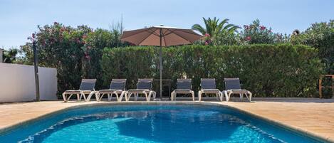 A swimming pool with lounge chairs and an umbrella.
