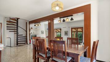 Un área de comedor con una mesa y sillas de madera, una escalera y una cocina visible a través de un arco.