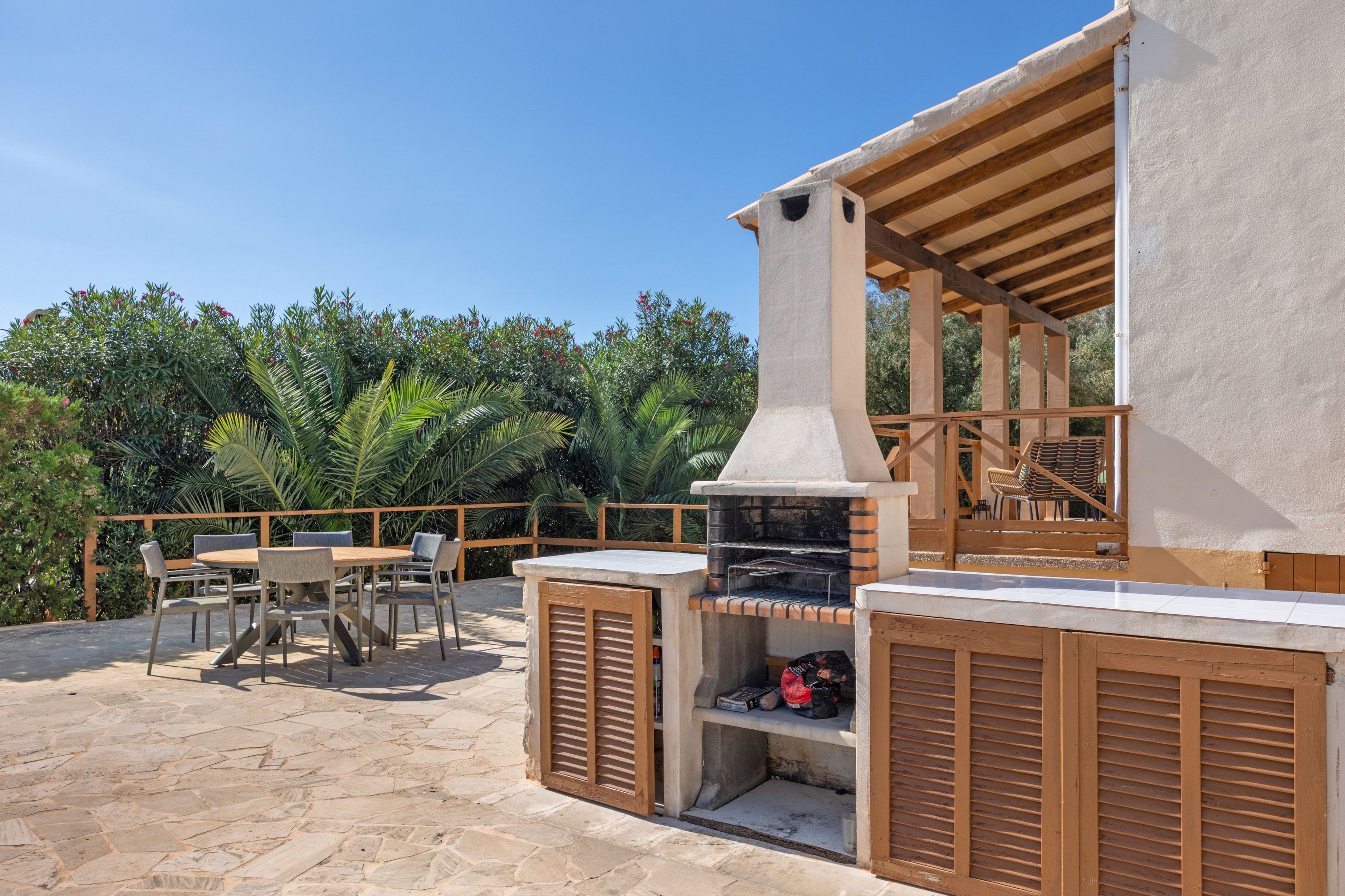 Eine Außenpatio mit Steinboden, einem Grill, Holzmöbeln und Blick auf üppiges Grün.