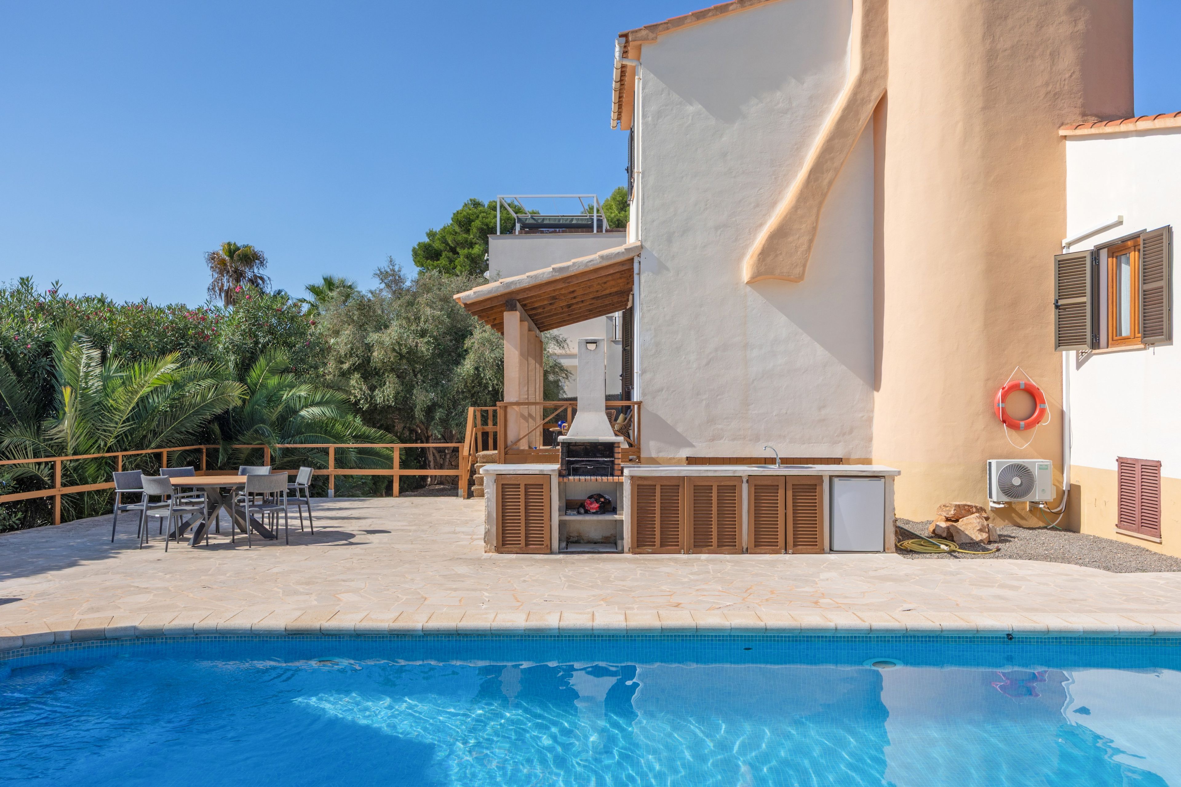 Zona junto a la piscina con una parrilla, asientos al aire libre y un flotador en la pared.