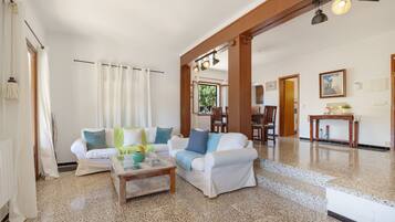 Amplia sala de estar con un conjunto de sofá blanco, una mesa de centro y un comedor con sillas y mesa de madera.