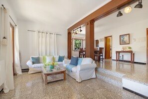 Un vaste espace de vie comprenant un canapé blanc, une table basse et un coin repas avec des chaises et une table en bois.