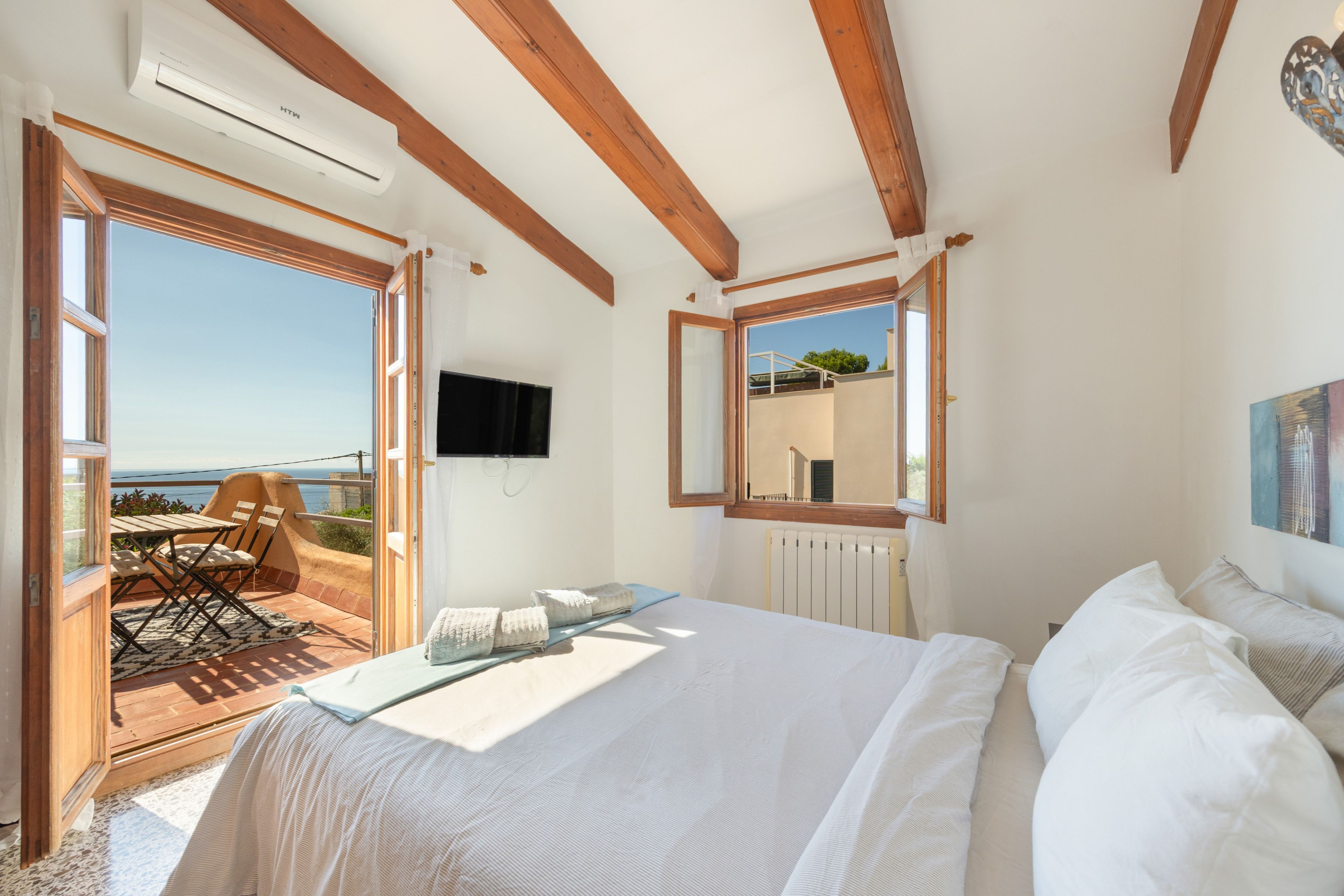 Un dormitorio con cama, televisor, ventana y balcón con vista al mar.