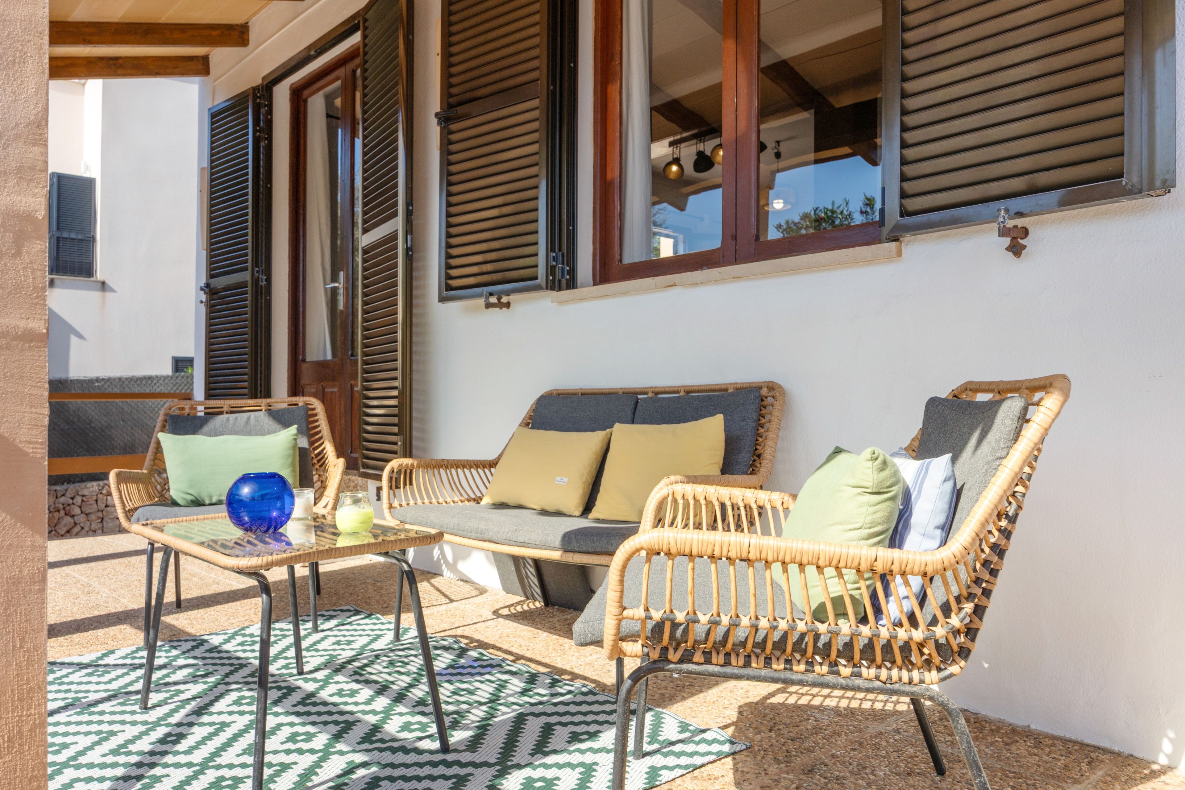 Un área de patio con mobiliario de mimbre, una mesa de vidrio y un tapete estampado.
