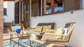 Un área de patio con mobiliario de mimbre, una mesa de vidrio y un tapete estampado.