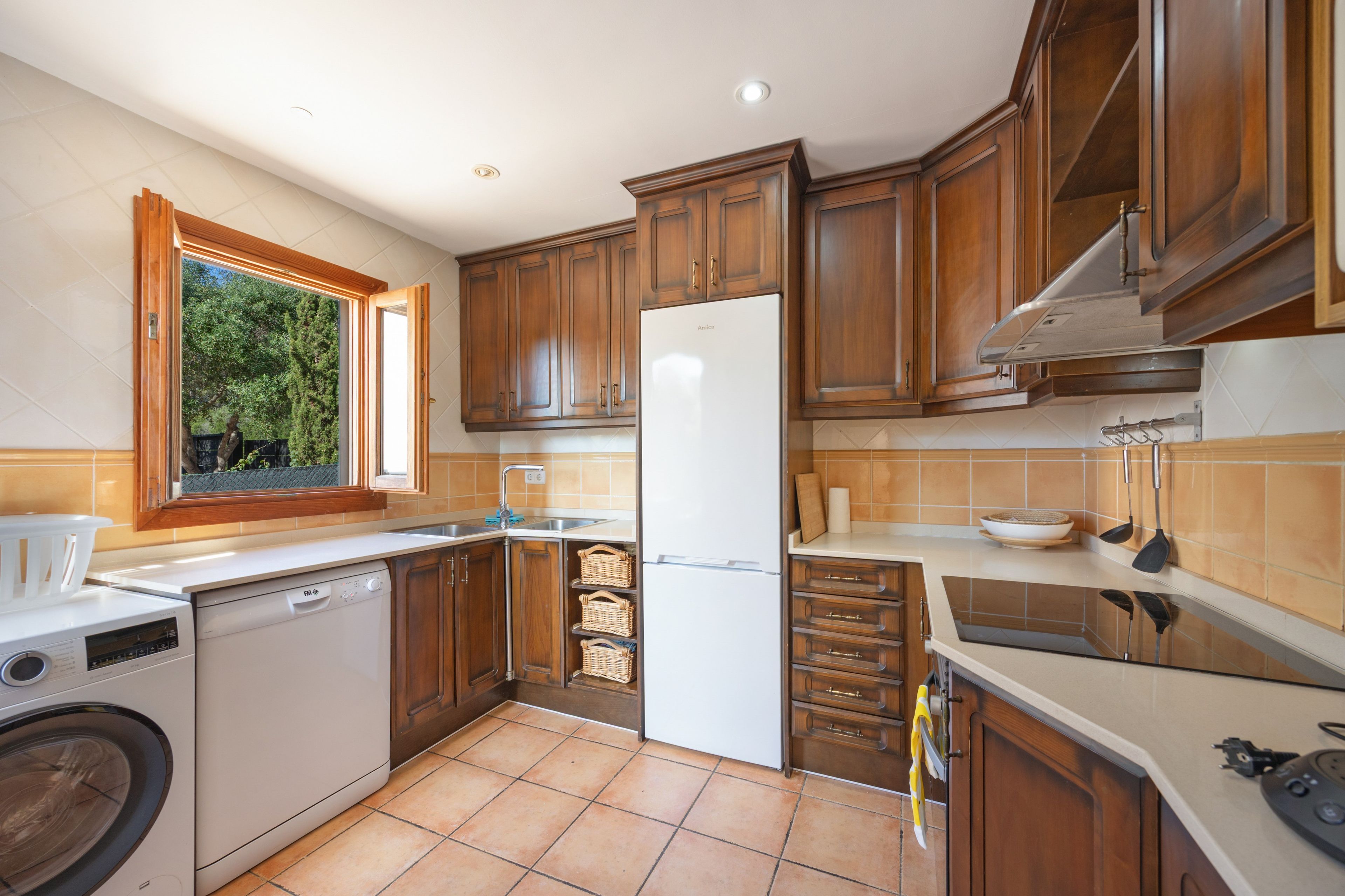 Una cocina con armarios de madera, un refrigerador blanco, un lavavajillas y una ventana con vista a follaje.