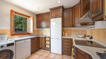 Una cocina con armarios de madera, un refrigerador blanco, un lavavajillas y una ventana con vista a follaje.