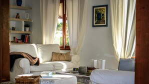 Un salon avec un canapé blanc, une table basse et une bibliothèque. On y trouve deux paniers en osier posés sur le sol.