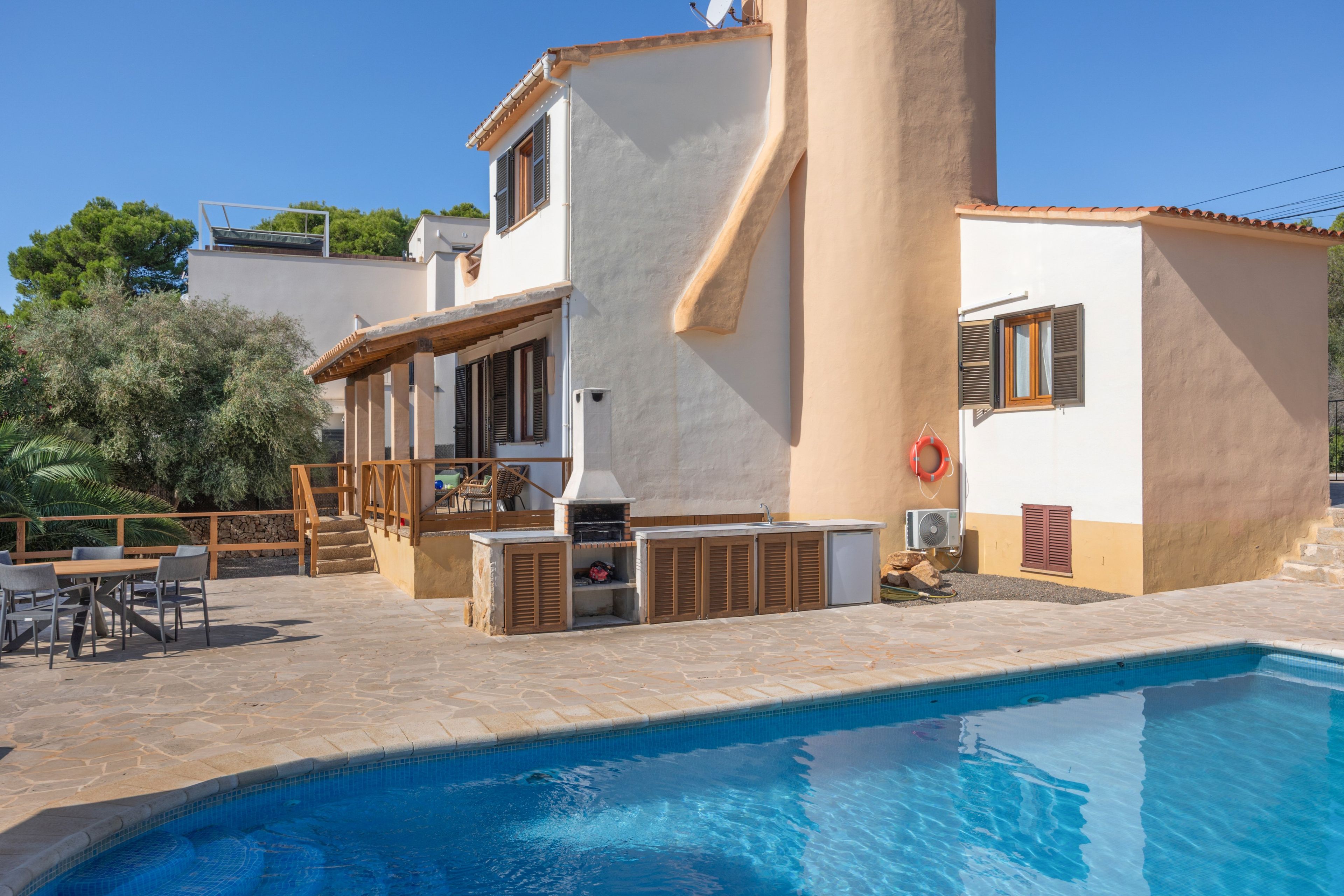Zona de piscina con patio de piedra, mobiliario exterior y una parrilla.