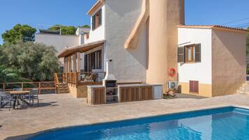 Zona de piscina con patio de piedra, mobiliario exterior y una parrilla.