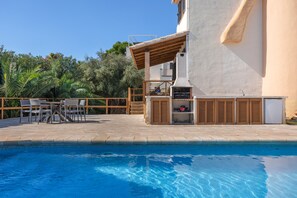 Un espace aménagé au bord de la piscine, comprenant un barbecue, des sièges d’extérieur et une vue sur la piscine.
