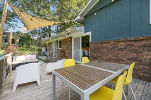 Une terrasse extérieure avec une table en bois et des chaises jaunes, un mur en briques et un espace salon abrité.