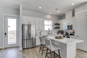 Una cocina moderna con armarios blancos, electrodomésticos de acero inoxidable y una isla central con taburetes de bar.