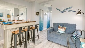 Ein modernes Wohnzimmer mit einem grauen Sofa, einer Sitzecke mit Holzbarhocker und einem großen Spiegel, der den Raum reflektiert.