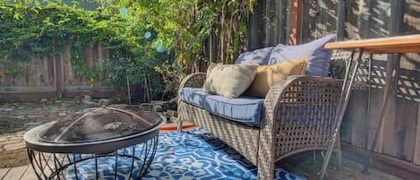 A wicker sofa with cushions, a fire pit, and a patterned rug on a wooden deck.