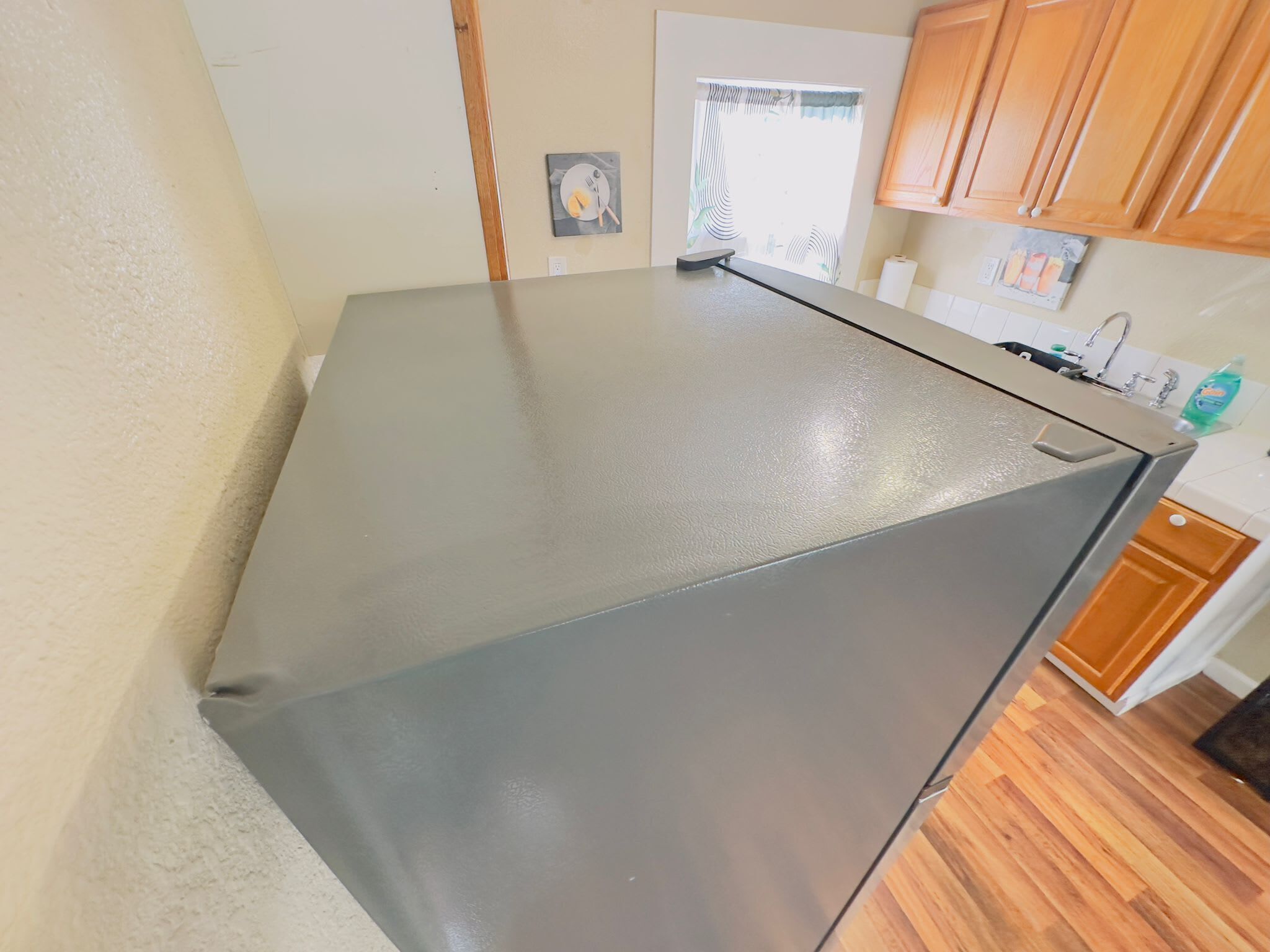 Una cocina con un refrigerador gris, armarios de madera y una ventana con cortinas.