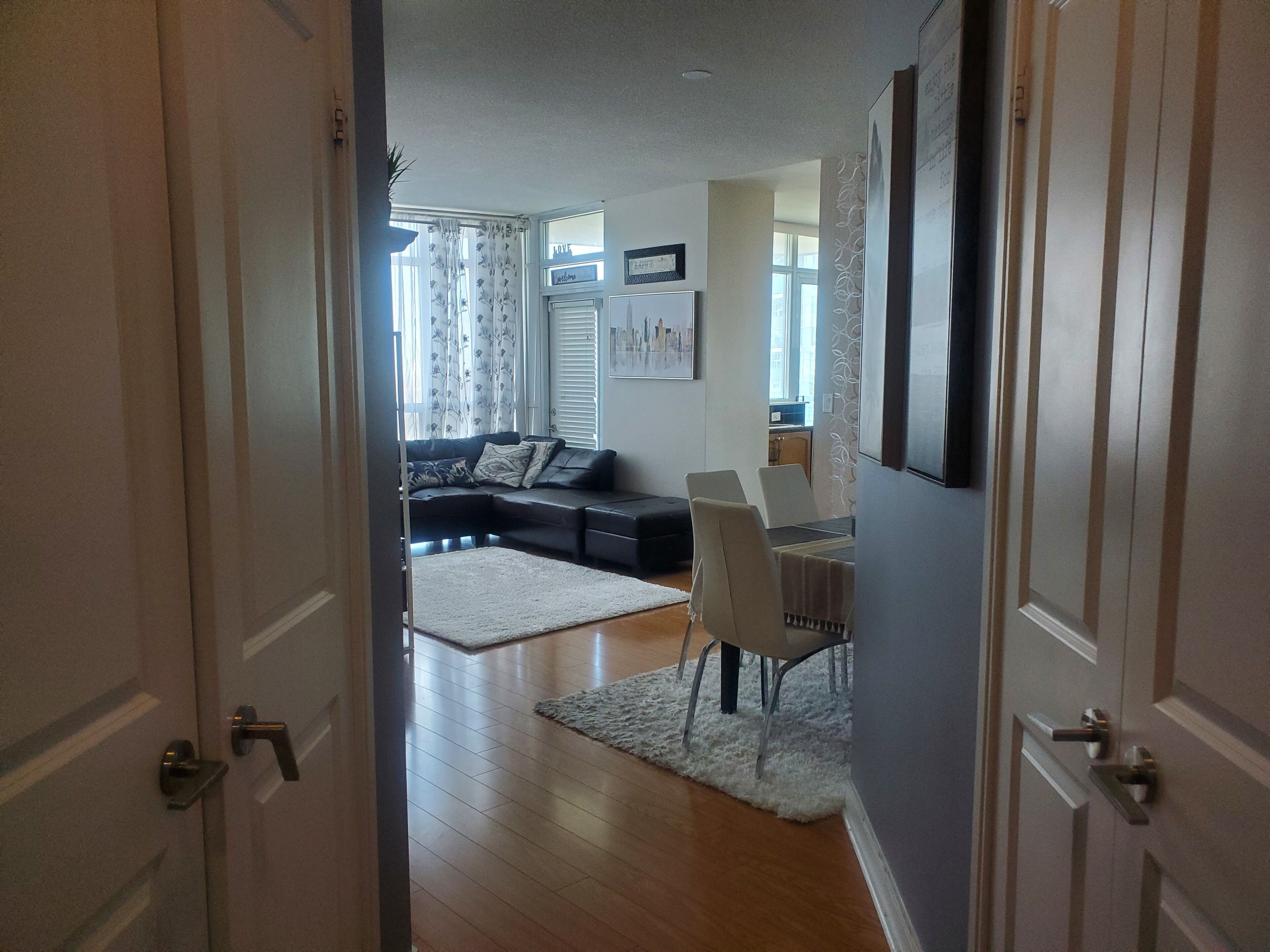 An open door leading to a living room with a sofa, a dining table with chairs, and a rug on the floor.