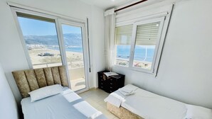 Una camera d'albergo con due letti, una piccola scrivania e vista sulla spiaggia e sulle montagne.