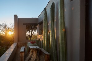 A balcony with a rustic wooden table, a cactus, and a view of the sunset.