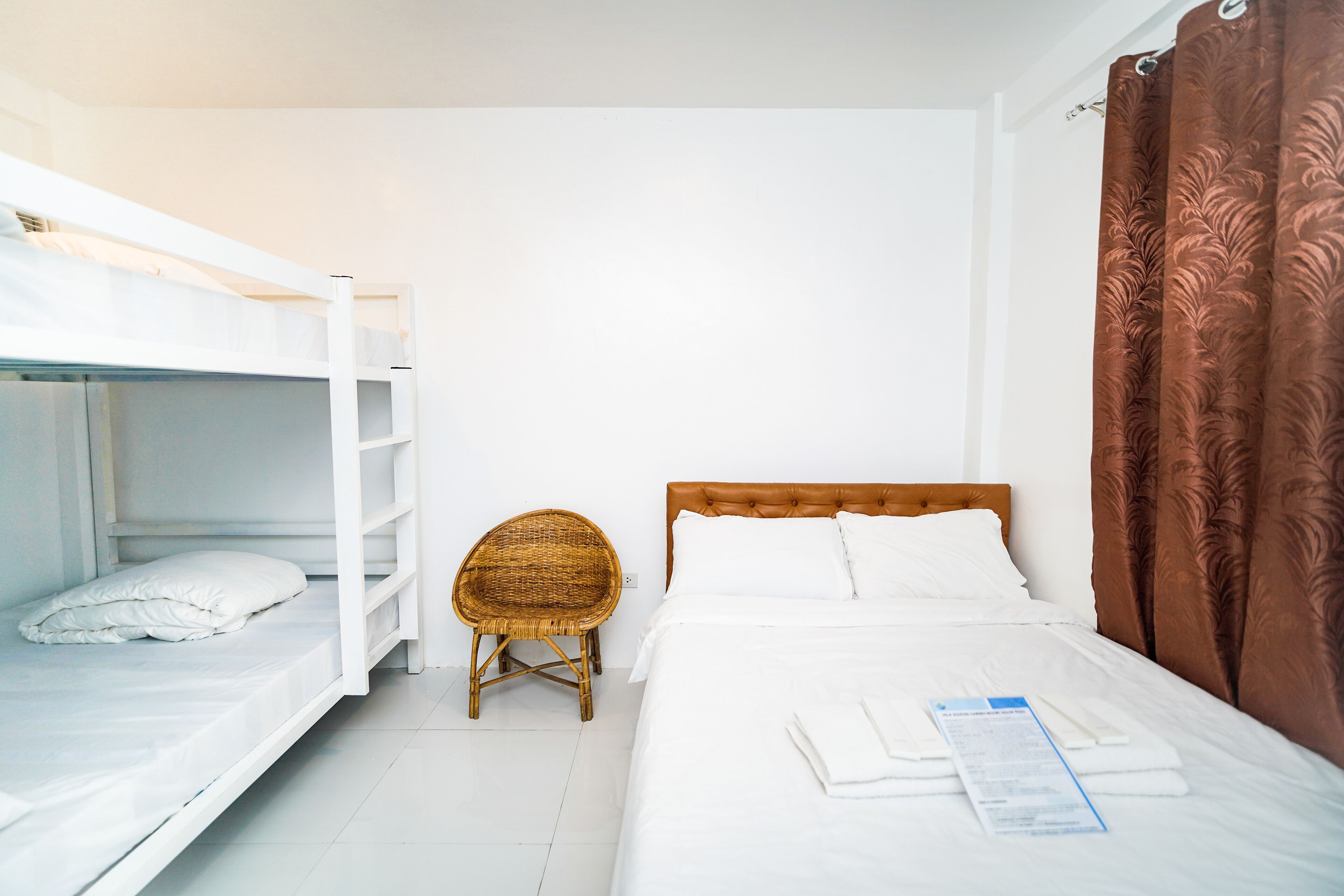 A room with a bunk bed, a single bed, a wicker chair, and a brown curtain.