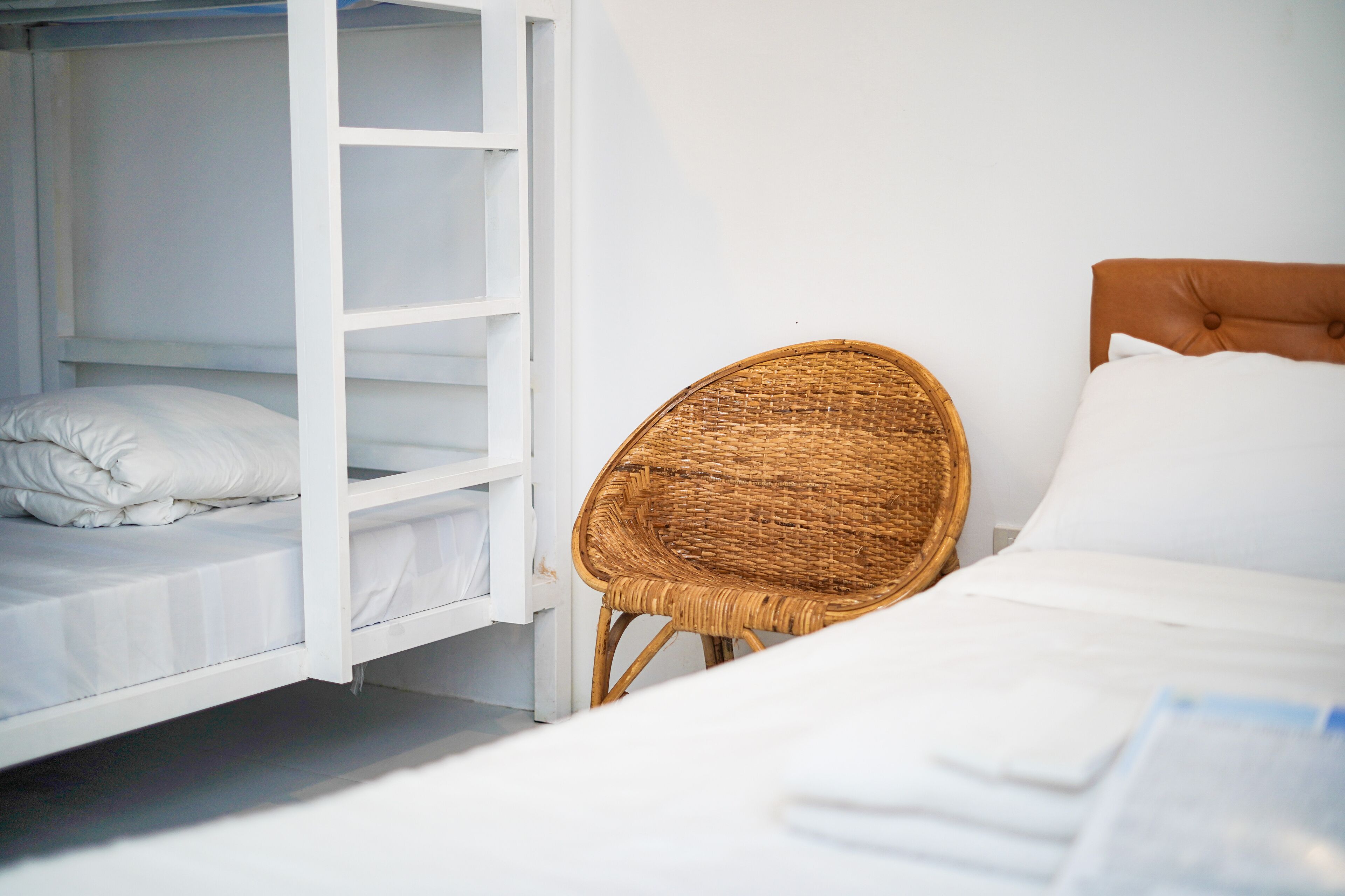 A bunk bed with white bedding, a wicker chair, and a headboard with a tufted design.