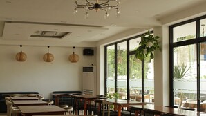 A spacious indoor dining area with long wooden tables and chairs, large windows offering a view of the outdoors, and a modern chandelier. - Villa Soledad Garden Resort (San Pablo)