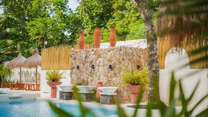 A pool area with a stone wall, terracotta pots, and thatched umbrellas. - Villa Soledad Garden Resort (San Pablo)