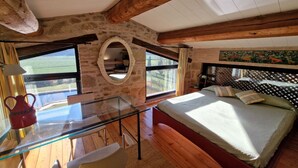 A bedroom with a glass table, a bed, a circular mirror, and large windows.