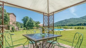 A covered patio with a table and chairs, a pool, and a mountainous landscape in the background.