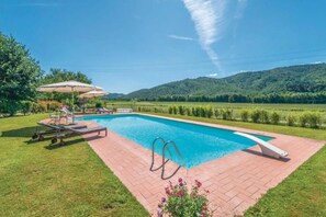 Une piscine rectangulaire bordée de briques, entourée de pelouse et agrémentée de quelques chaises longues.