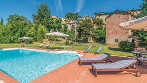 A swimming pool with lounge chairs and umbrellas, surrounded by greenery and buildings.