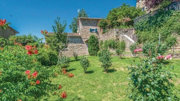 A stone building with a small window, surrounded by lush greenery and flowering plants.