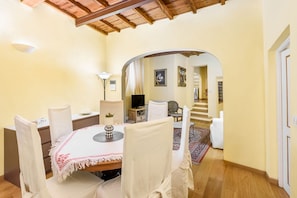 A dining area with a round table, chairs, a television, and a staircase leading to another room.