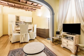 A compact living space with a kitchenette, a dining area with chairs, a TV stand, and a patterned rug.