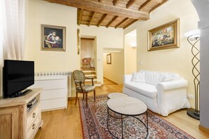 A living room with a television, white sofa, patterned rug, wooden floor, and a staircase leading to another room.