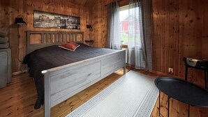 A wooden cabin bedroom with a bed, a chair, a desk, and a cityscape painting on the wall. - Amazing home in Kinnahult with WiFi (Kinnahult)