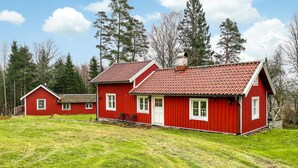 A red wooden house with a tiled roof, surrounded by a grassy field and trees. - Amazing home in Kinnahult with WiFi (Kinnahult)
