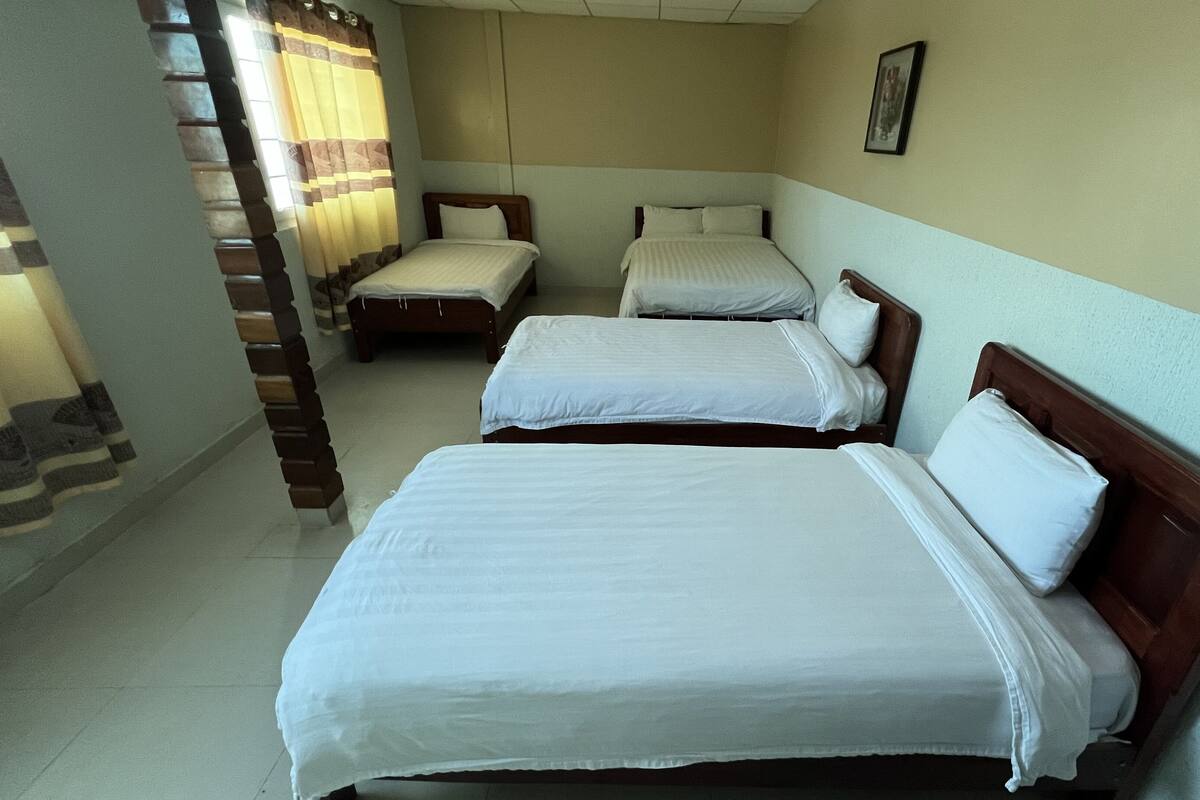 A hotel room with three single beds, a wooden headboard, a small bedside table, and a curtain.