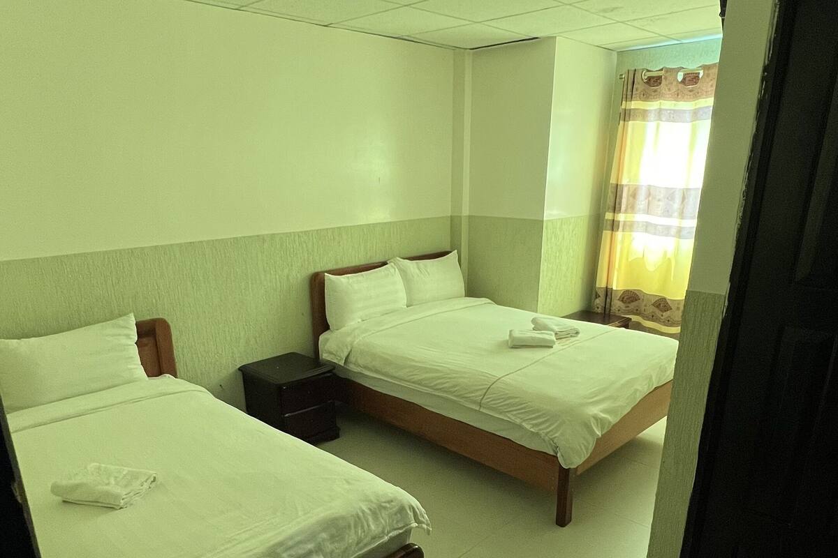 A hotel room with two single beds, a nightstand, a window with curtains, and a door.
