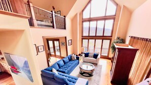A spacious living room with a large sectional sofa, a coffee table, and a view of the outdoors through large windows. - Tranquil Waters Retreat: Hot Tub, Pool & Lake Views (Smithville)